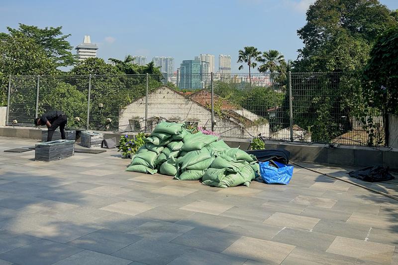 Bags of soil mix and new planters delivered to the roof terrace, a worker unpacking in the distance.