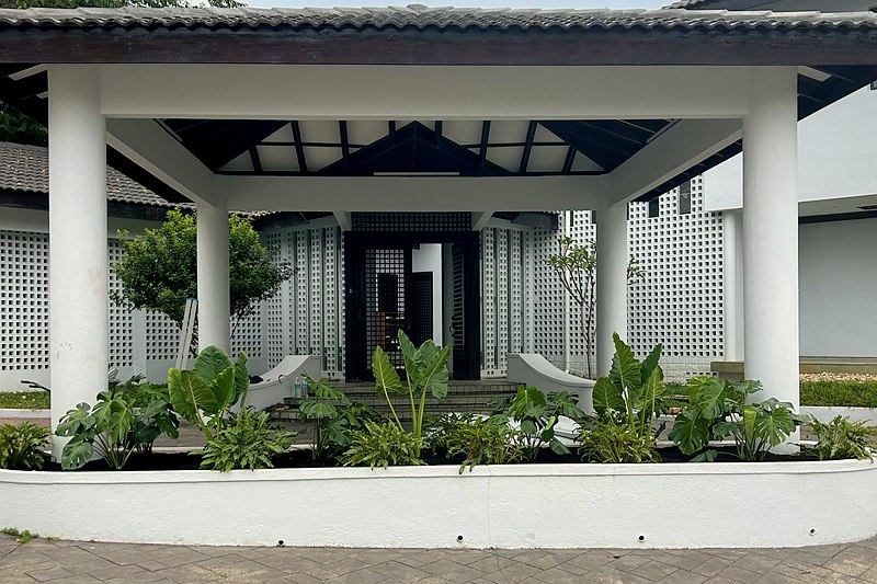 White columned entrance porch with a curved planter of elephant ears, Monstera and philodendron in front of breeze-block walls